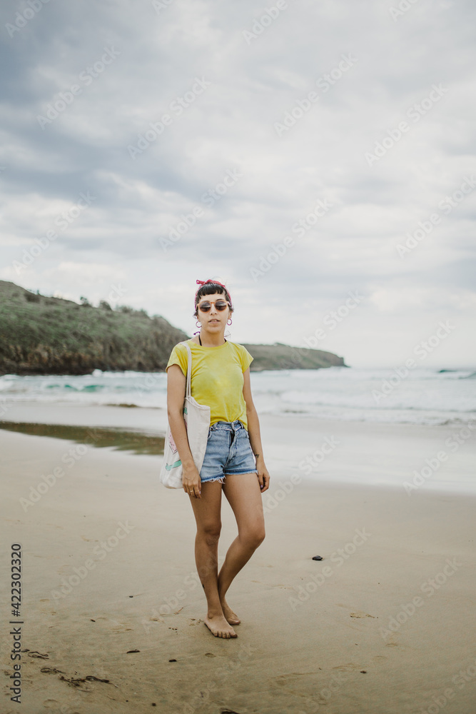 plano entero de mujer joven posando con pantalones cortos remera amarilla y gafas de sol, posando en la playa mirando hacia la camara plano entero de mujer joven posando con pantalones cortos remera amarilla y gafas de sol, posando en la playa mirando hacia la camara