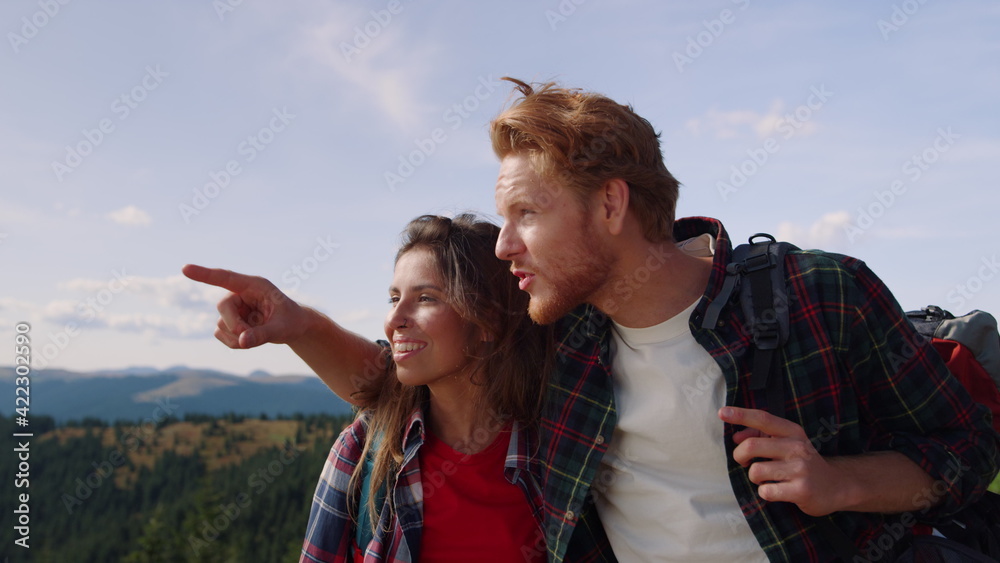 Woman and man standing on top of mountain. Male hiker pointing finger away
