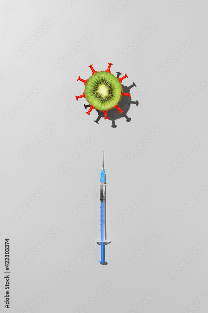 Concept of vaccination against coronavirus. Top view of syringe with vaccine against COVID-19 and half kiwi fruit in the form of virus on gray background Concept of vaccination against coronavirus. Top view of syringe with vaccine against COVID-19 and half kiwi fruit in the form of virus on gray background