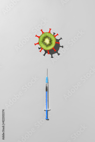Concept of vaccination against coronavirus. Top view of syringe with vaccine against COVID-19 and half kiwi fruit in the form of virus on gray background