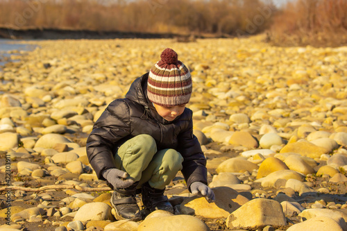 Little boy playing with pebbles on the banks of a mountain river. Active recreation in nature.