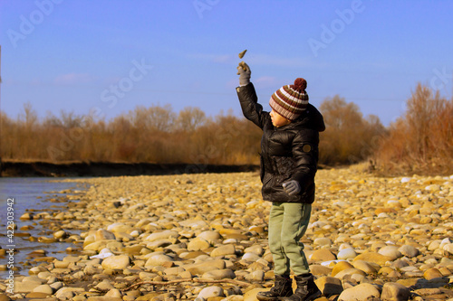 A little boy throws pebbles into the river. Active recreation in nature.