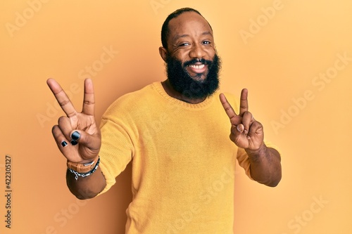 Young african american man wearing casual clothes smiling looking to the camera showing fingers doing victory sign. number two.