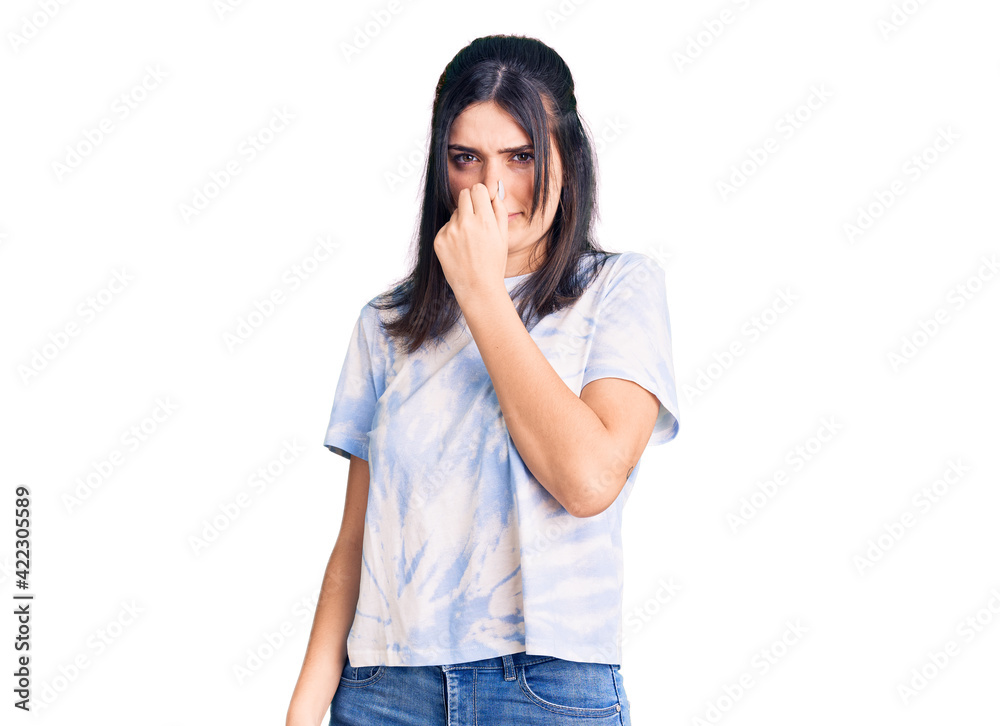 Young beautiful girl wearing casual t shirt smelling something stinky and disgusting, intolerable smell, holding breath with fingers on nose. bad smell Young beautiful girl wearing casual t shirt smelling something stinky and disgusting, intolerable smell, holding breath with fingers on nose. bad smell