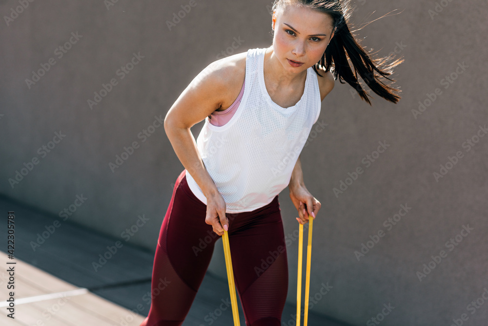 Sporty young woman exercising with resistance band on a sunny day. Athlete female working out with elastic bands outside. Sporty young woman exercising with resistance band on a sunny day. Athlete female working out with elastic bands outside.