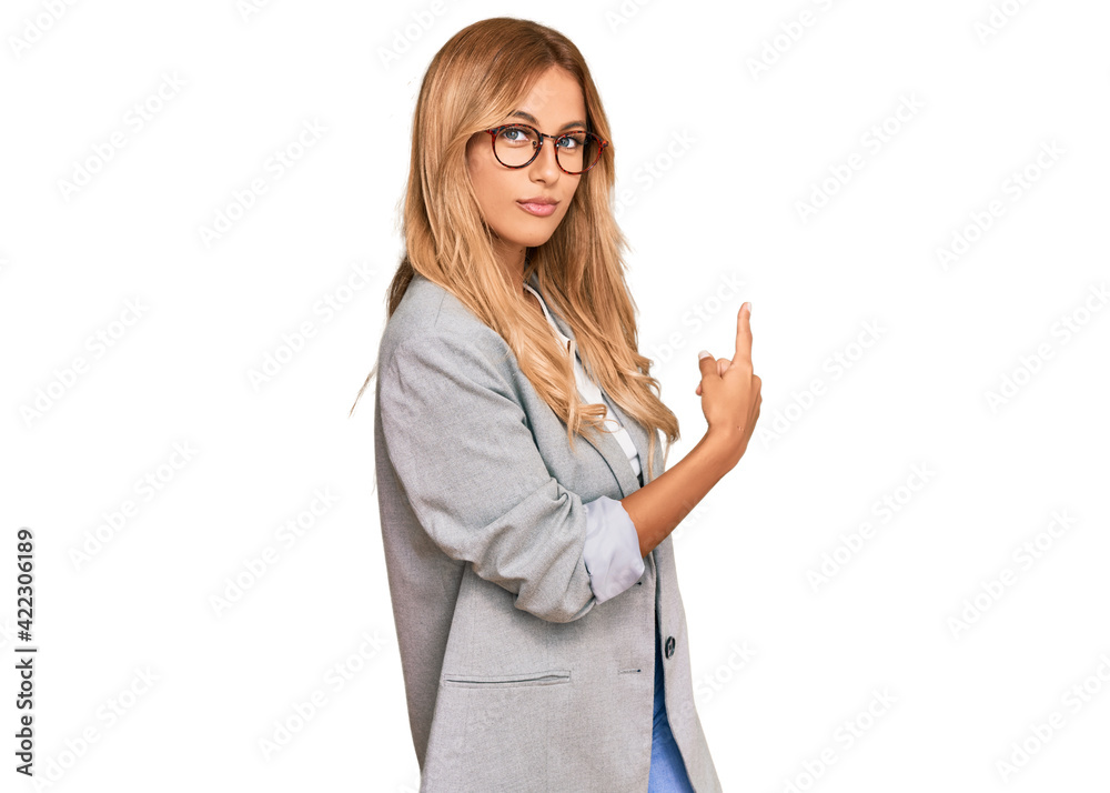 Beautiful blonde young woman wearing business clothes pointing with hand finger to the side showing advertisement, serious and calm face Beautiful blonde young woman wearing business clothes pointing with hand finger to the side showing advertisement, serious and calm face