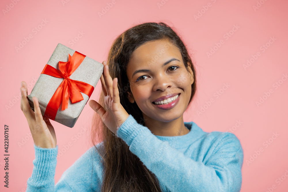 Excited african woman received gift box with bow. She is happy and flattered by attention. Girl smiling with present on pink background. Studio portrait Excited african woman received gift box with bow. She is happy and flattered by attention. Girl smiling with present on pink background. Studio portrait