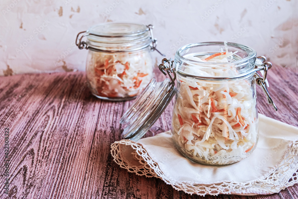 Two glass jars filled with homemade sauerkraut with carrots on wooden table. Fermented vegetables. Vegetarian vegan food. Fermented cabbage, german and russian style cuisine. Copy space. Two glass jars filled with homemade sauerkraut with carrots on wooden table. Fermented vegetables. Vegetarian vegan food. Fermented cabbage, german and russian style cuisine. Copy space.