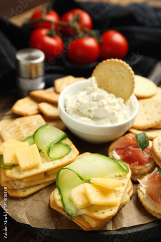 Different snacks with salted crackers on wooden board, closeup