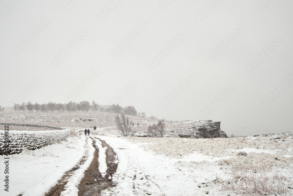 Snow falling, people walking along Froggatt Edge, Peak District, UK