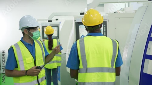 Caucasian male supervisor wear face mask checking Asian and Africa workers in factory production line. Concept of new normal working in Covid-19 pandemic and diversity.