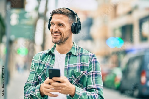 Young caucasian man smiling happy using smartphone and headphones at the city.