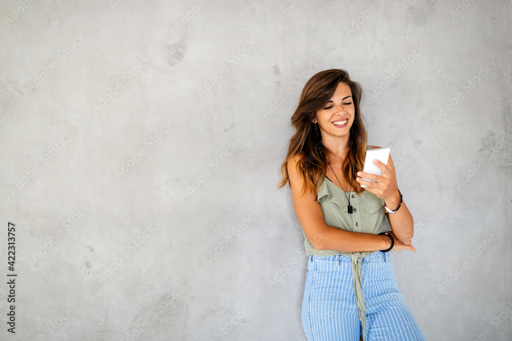 Portrait of laughing young woman with mobile phone standing against a gray wall Portrait of laughing young woman with mobile phone standing against a gray wall