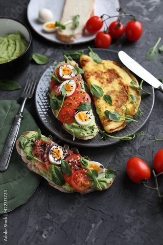 Delicious and healthy breakfast. Toast with fish, avocado and quail eggs on a plate with omelet. Proper nutrition.