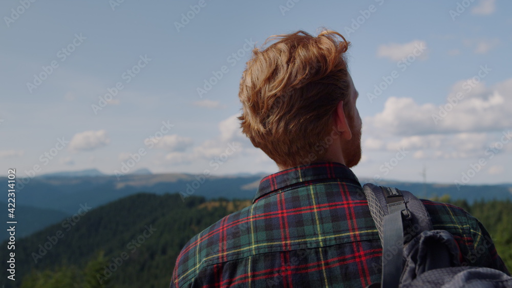 Male hiker standing on top of mountain. Redhead man looking summer landscape