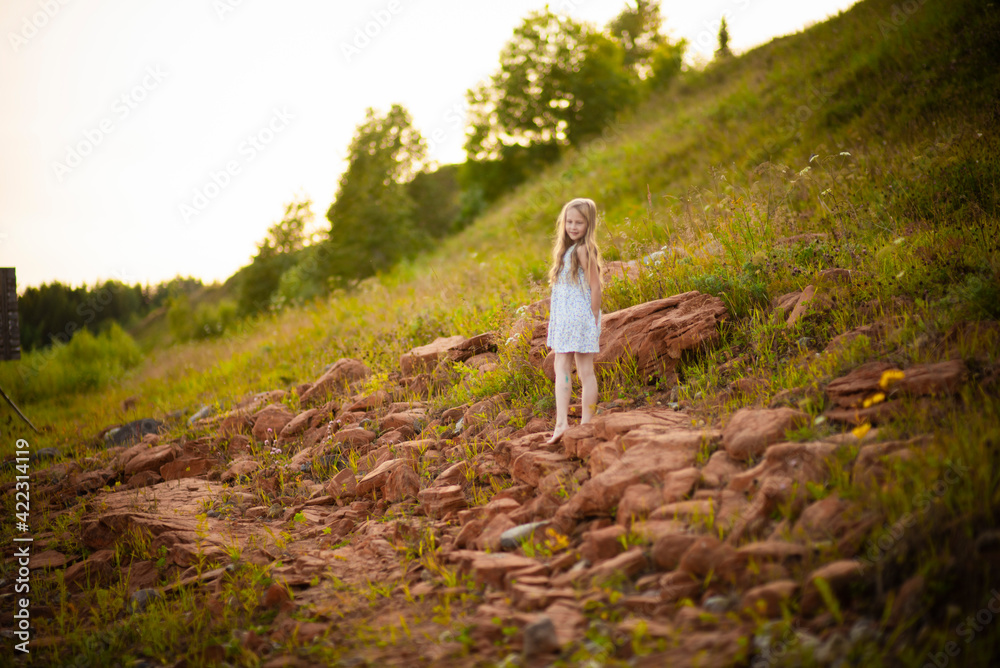 blonde girl in a sundress on red stones, selective focus