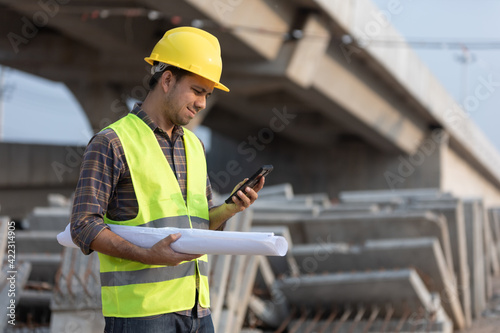Asian construction workers use smartphone and hold a plan blueprint at the construction site
