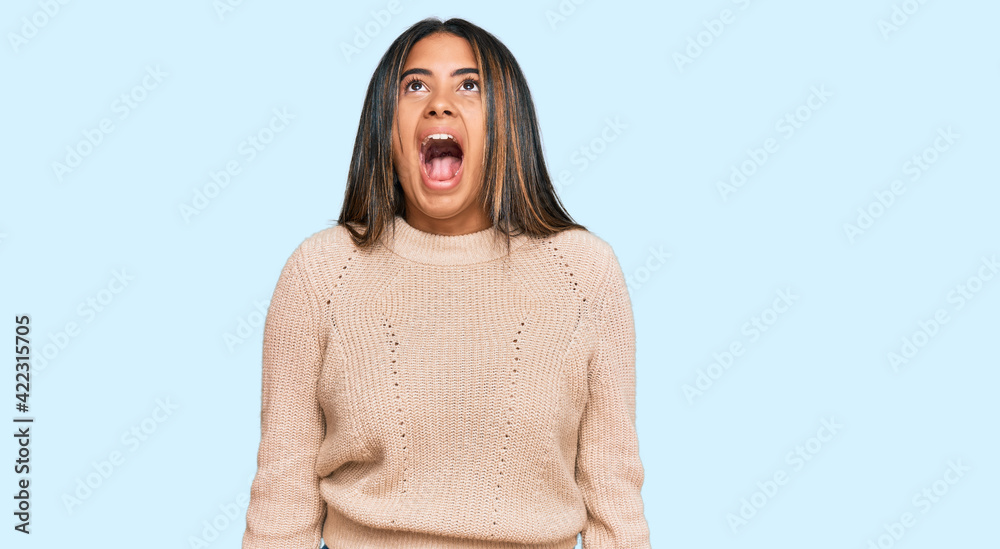 Young latin girl wearing wool winter sweater angry and mad screaming frustrated and furious, shouting with anger. rage and aggressive concept. Young latin girl wearing wool winter sweater angry and mad screaming frustrated and furious, shouting with anger. rage and aggressive concept.