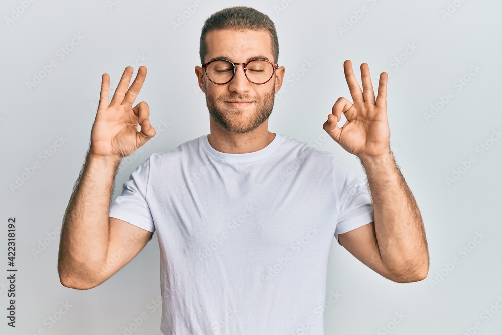 Fototapeta premium Young caucasian man wearing casual clothes and glasses relax and smiling with eyes closed doing meditation gesture with fingers. yoga concept.