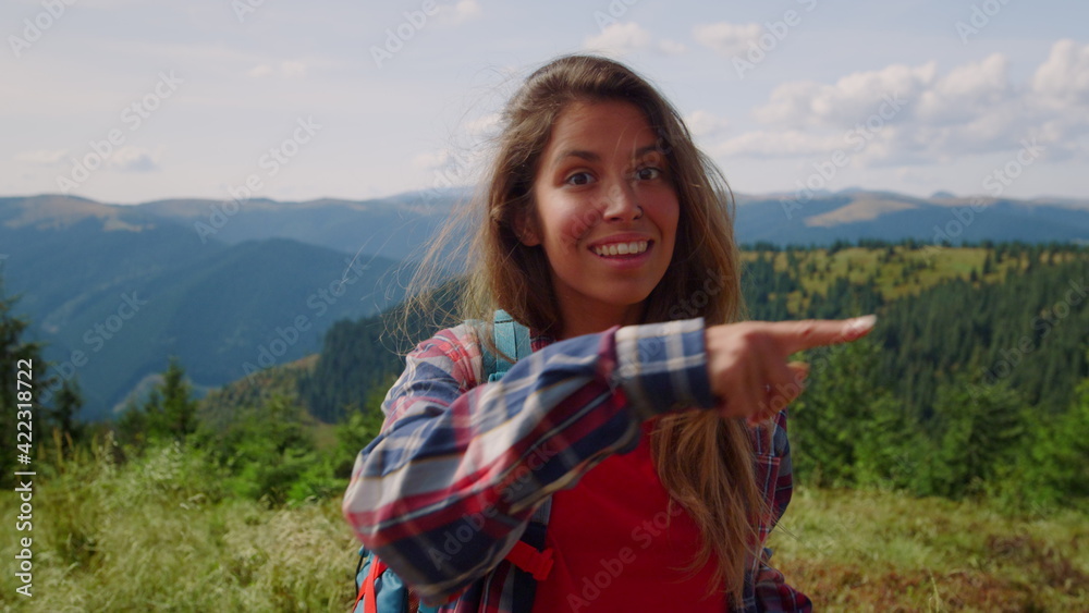 Smiling woman looking at camera in mountains. Female tourist wearing backpack