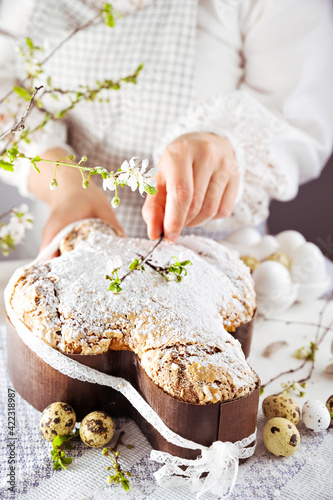 In hand Traditional Italian desserts for Easter - Easter dove . Festive pastries with almonds and sugar icing on a light background and flowering branches, Easter decor and eggs. vertical 