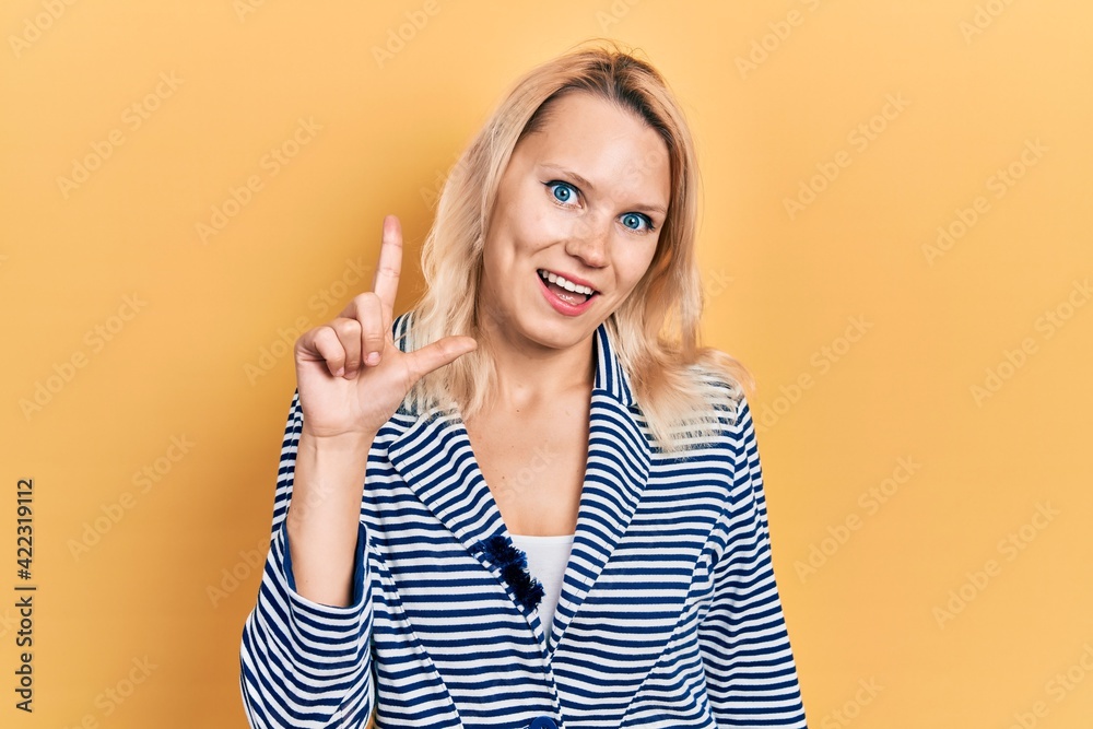 Beautiful caucasian blonde woman wearing business jacket smiling with an idea or question pointing finger up with happy face, number one