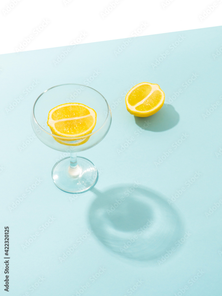 Minimal summer scene with halved lemon in crystal champagne glass on bright blue table.