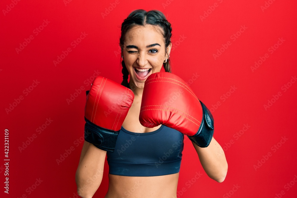 Young brunette girl using boxing gloves winking looking at the camera with sexy expression, cheerful and happy face.