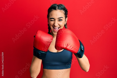 Young brunette girl using boxing gloves winking looking at the camera with sexy expression, cheerful and happy face. © Krakenimages.com