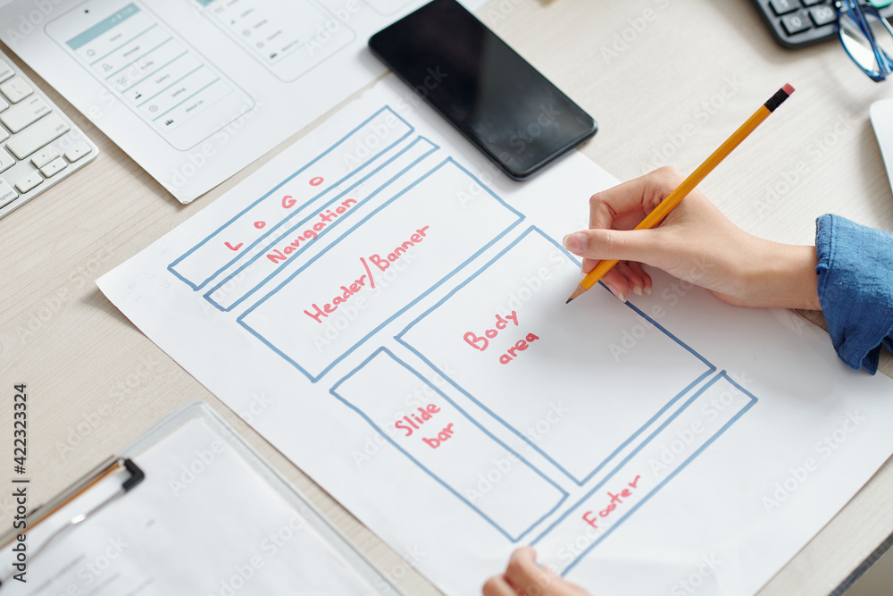 Hands of creative UI designer drawing mobile application interface layout on paper sheet Hands of creative UI designer drawing mobile application interface layout on paper sheet