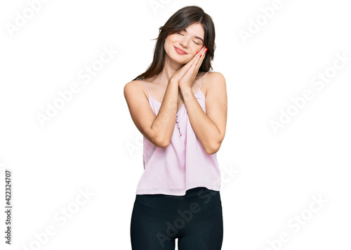 Young beautiful caucasian girl wearing casual clothes sleeping tired dreaming and posing with hands together while smiling with closed eyes.