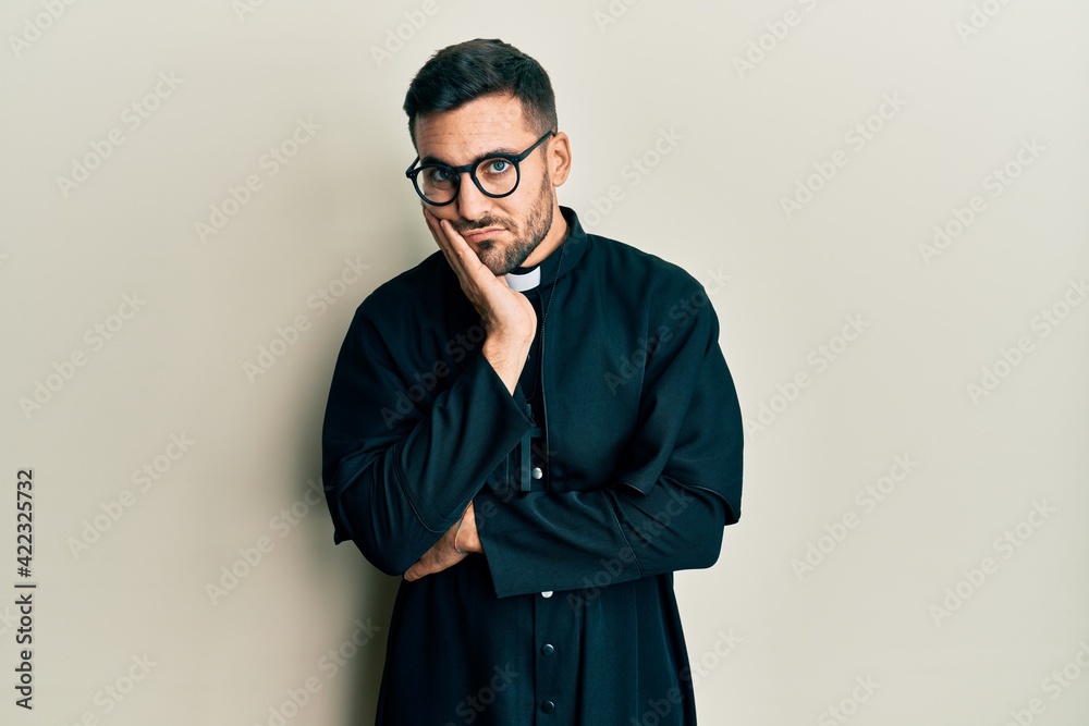 Young hispanic man wearing priest uniform standing over white background thinking looking tired and bored with depression problems with crossed arms.