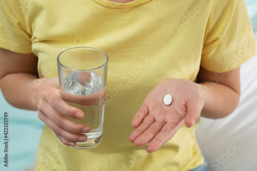 Young woman with abortion pill and glass of water on blurred background, closeup