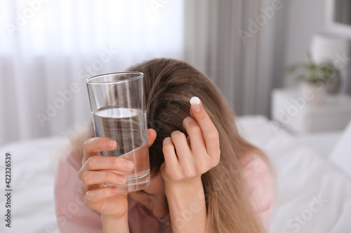 Upset young woman with abortion pill and glass of water at home