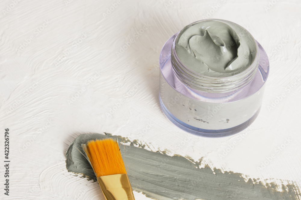 a brush for applying face masks, a jar of cosmetic blue clay and a smear of clay on a textured light background copy space a brush for applying face masks, a jar of cosmetic blue clay and a smear of clay on a textured light background copy space