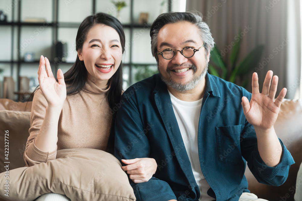 Portrait of Asian mature couple sitting and smiling in living room. wife woman hand hold husband arm from behind and look at camera with happiness and cheerful safty amd insurance family concept Portrait of Asian mature couple sitting and smiling in living room. wife woman hand hold husband arm from behind and look at camera with happiness and cheerful safty amd insurance family concept