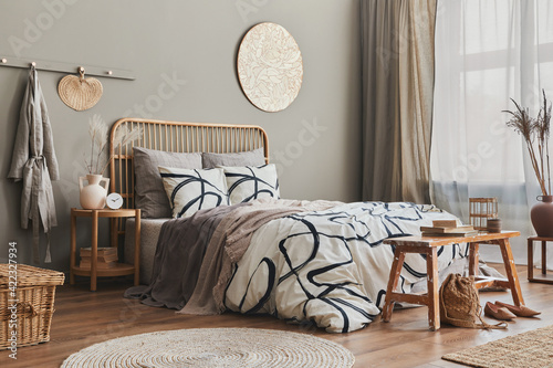 Stylish composition of bedroom interior with wooden bed, furniture, dried flowers in vase, rattan decoration, vases and elegant accessories. Beautiful bed sheets, blanket and pillows. Cozy home decor. photo