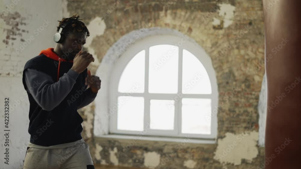Afro american male boxer practicing shadow boxing in headphones in bright hall Afro american male boxer practicing shadow boxing in headphones in bright hall
