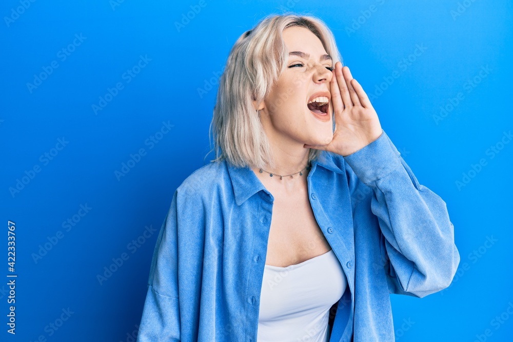 Young blonde girl wearing casual clothes shouting and screaming loud to side with hand on mouth. communication concept. Young blonde girl wearing casual clothes shouting and screaming loud to side with hand on mouth. communication concept.