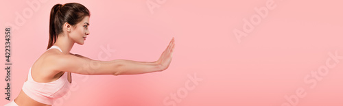 Side view of fit sportswoman exercising isolated on pink, banner