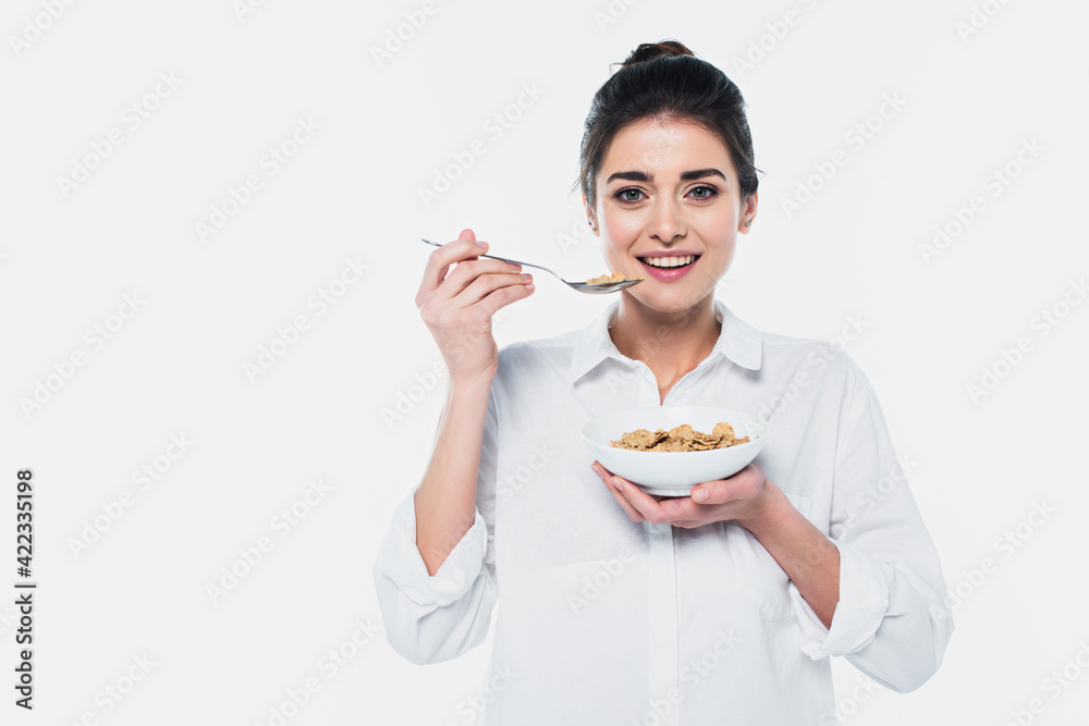 Smiling brunette woman holding spoon and bowl of cereals isolated on white Smiling brunette woman holding spoon and bowl of cereals isolated on white