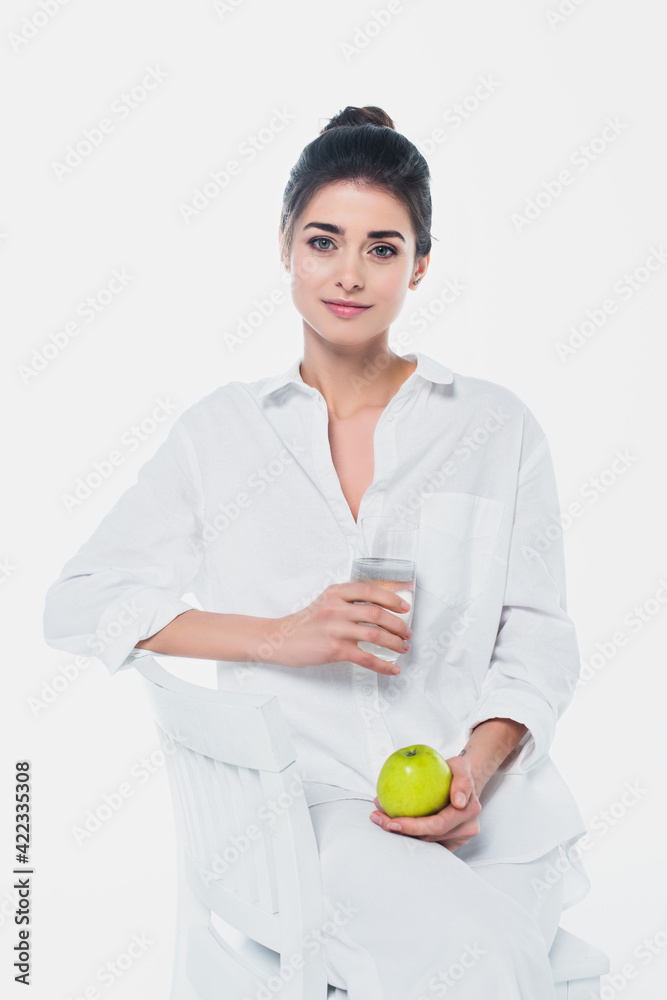 Pretty woman with glass of water and organic apple sitting on chair isolated on white Pretty woman with glass of water and organic apple sitting on chair isolated on white