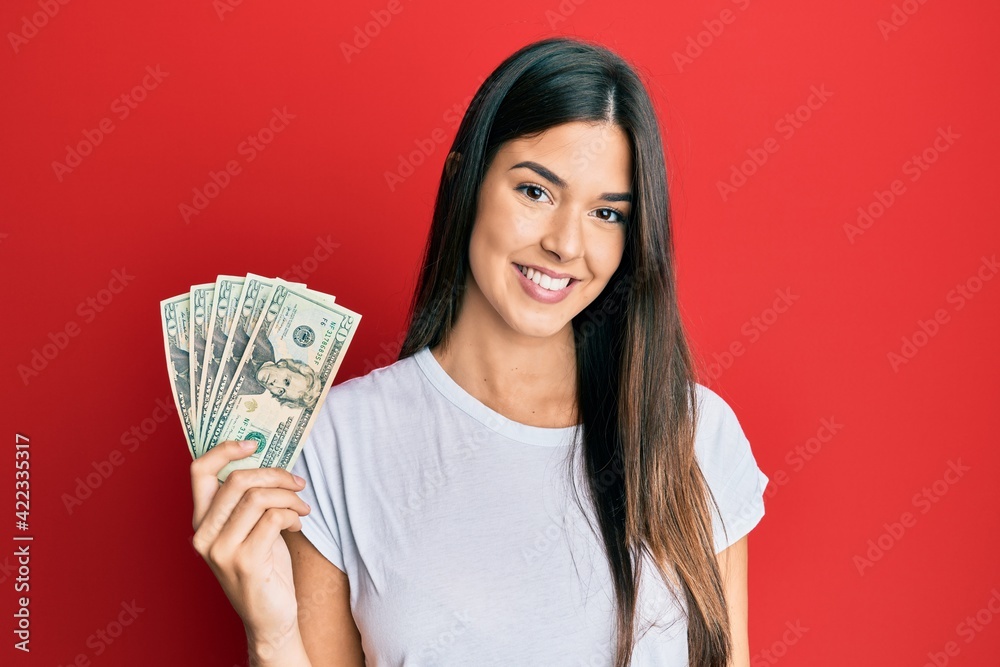 Young brunette woman holding 20 dollars banknote looking positive and happy standing and smiling with a confident smile showing teeth Young brunette woman holding 20 dollars banknote looking positive and happy standing and smiling with a confident smile showing teeth