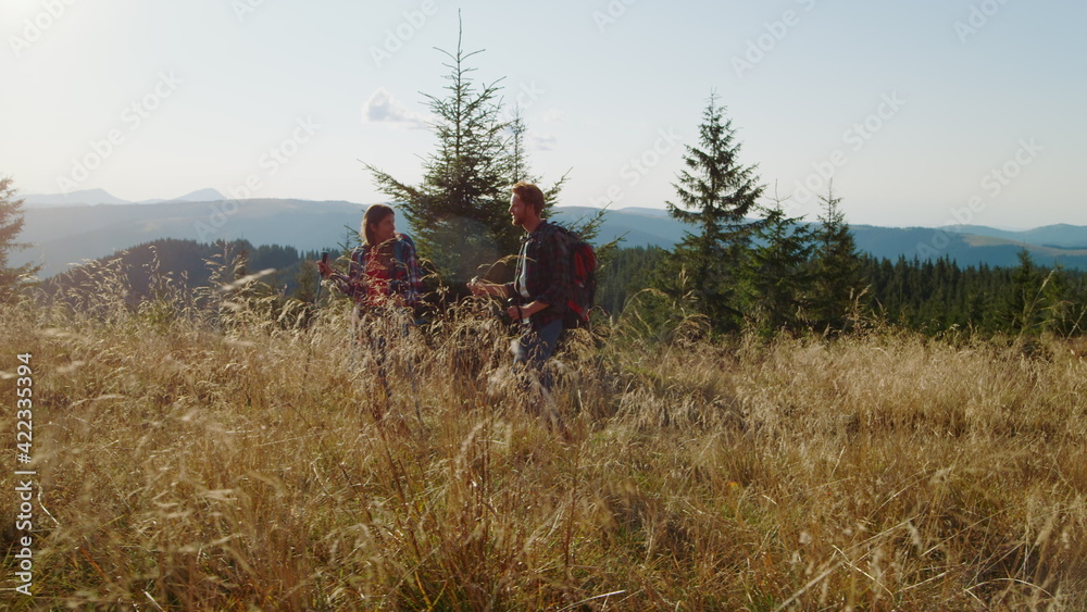 Obraz premium Smiling guy and girl hiking on road in field. Tourists trekking in mountains