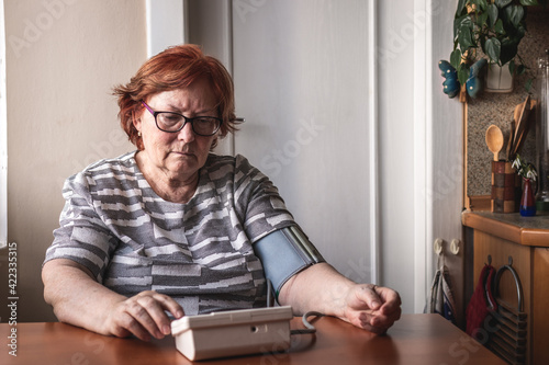 Worried senior woman checking her blood pressure by medical device. Everyday life of old people with hypertension illness diagnosis