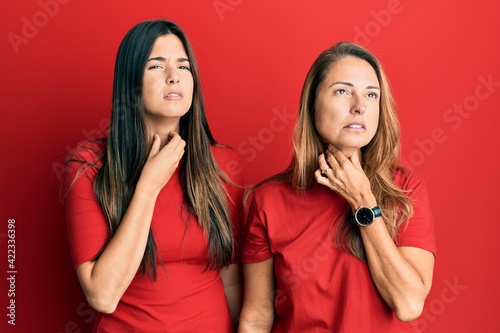 Hispanic family of mother and daughter wearing casual clothes over red background touching painful neck, sore throat for flu, clod and infection