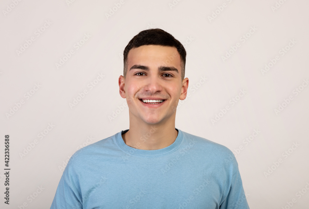 Obraz premium Portrait of handsome Caucasian young man in casual clothes smiling and looking at camera over light grey background