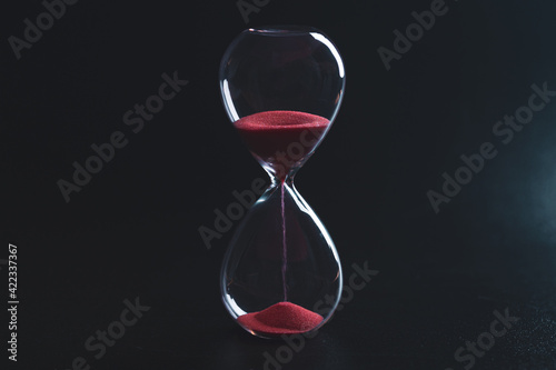 Sand passes through an hourglass, measuring the travel time counting down to the deadline, against a dark background with space for text