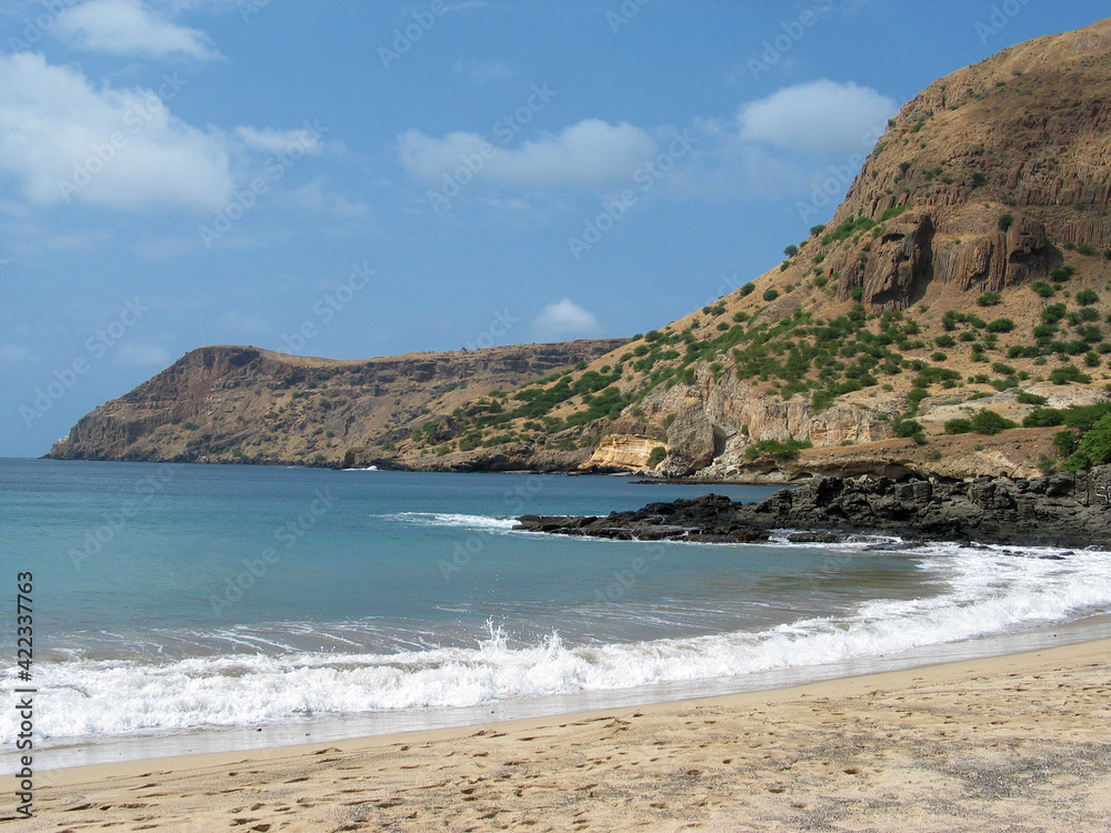 Empty beach in Cabo Verde Islands, white sand, surf, blue water and rolling volcanic hills.