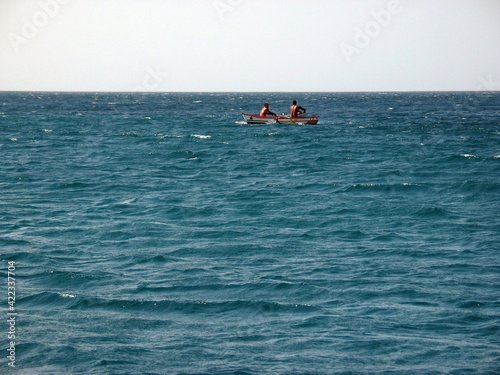 Athlets competing in a small rowing boat, blue ocean water in foreground and background, Cabo Verde Islands.